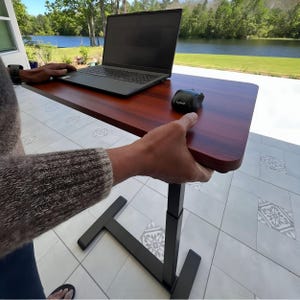 May include: A black laptop computer sits on a wooden standing desk with a black wireless mouse. The desk has a black metal frame and is adjustable in height.