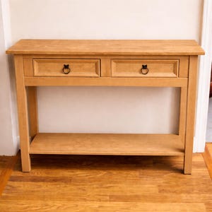 May include: A light oak console table with two drawers and a lower shelf. The drawers have black ring pulls. The table is made of wood and has a natural finish. The table is 48 inches wide, 16 inches deep, and 30 inches high.