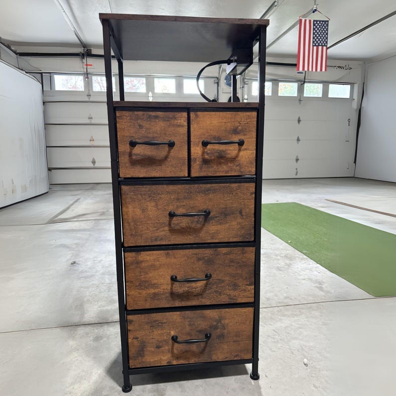 May include: A five-drawer wooden chest with a black metal frame. The drawers have black metal handles and are made of a light brown wood with a distressed finish. The chest has a small shelf on top.