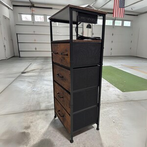 May include: A brown and black metal 4-drawer dresser with a black top shelf. The top shelf has a built-in power strip with a cord hanging down.
