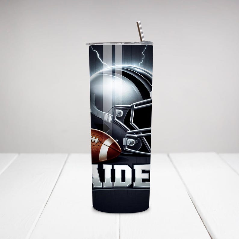 May include: A black and silver stainless steel tumbler with a football helmet and football graphic. The tumbler has a white stripe down the side and the word "RAIDERS" printed on the bottom.