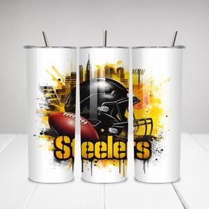 Op de afbeelding: Witte beker met een footballhelm en football, met een stadsgezicht en gele en zwarte accenten. Het woord "Steelers" wordt in grote, gele letters weergegeven. De beker heeft een zilveren rietje.