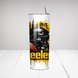 Op de afbeelding: Een roestvrijstalen beker met een footballhelm en football met een skyline-achtergrond. Het woord "Steele" wordt in geel en zwart weergegeven. De beker heeft een zilveren rietje en een witte achtergrond.