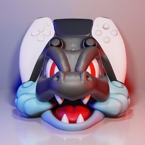 Puede incluir: Soporte personalizado para mando de videojuegos con diseño de dragón estilizado. El soporte es principalmente negro, gris y azul, con detalles rojos en ojos y boca. El mando es blanco y negro.