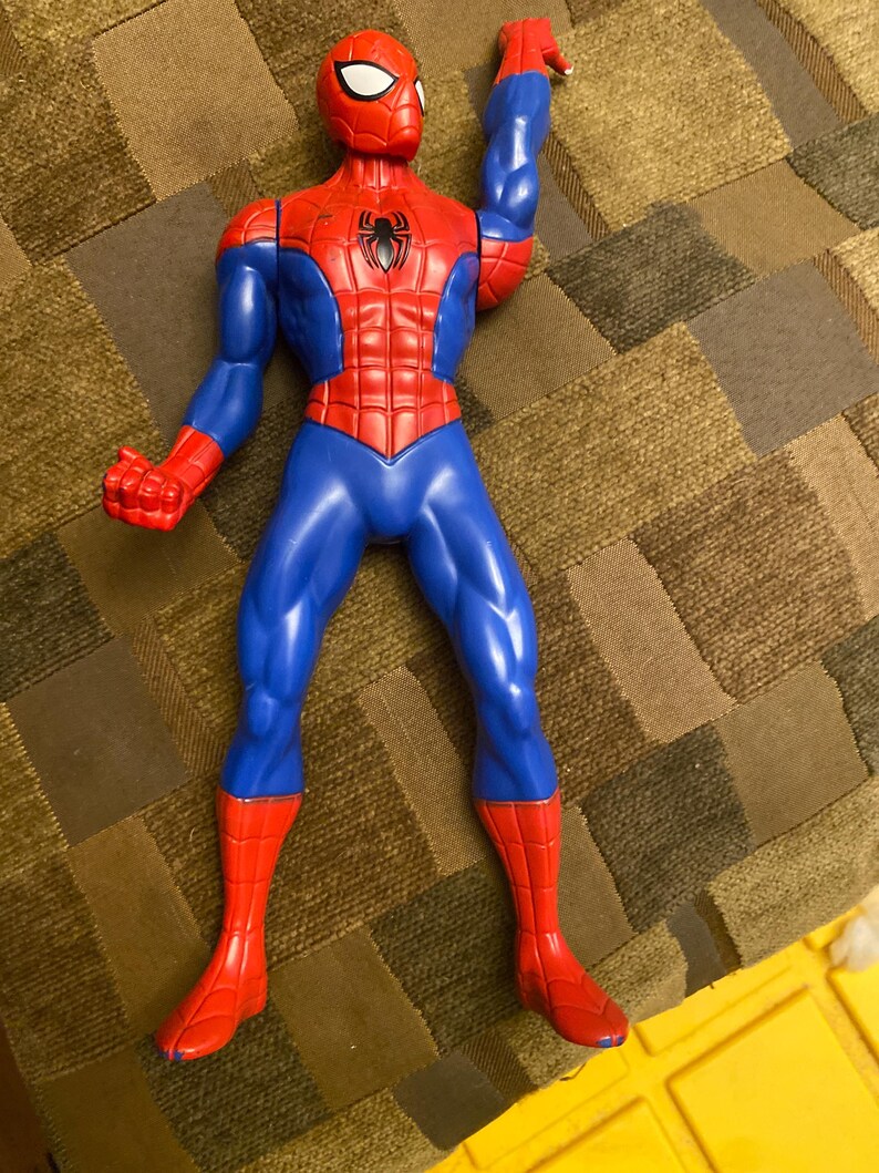 May include: A plastic Spider-Man action figure in a dynamic pose. The figure features a red and blue color scheme, with a red mask, torso, and boots, and blue arms and legs. A black spider emblem is on the chest.