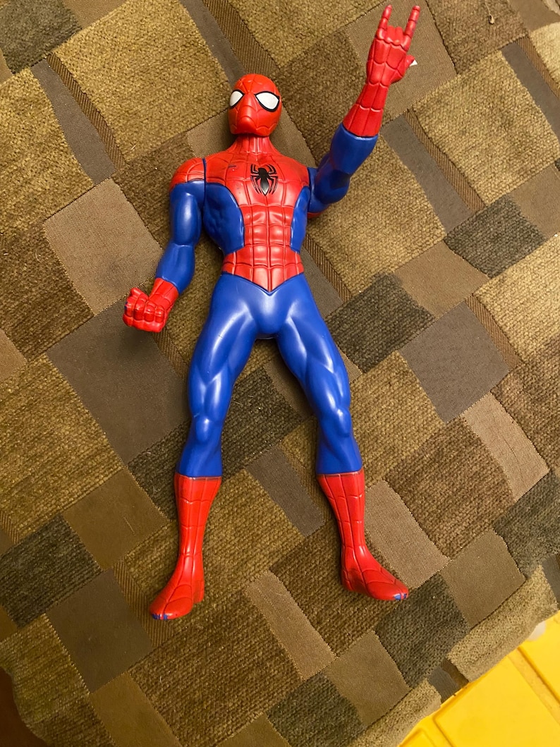 May include: A Spider-Man action figure in a classic red and blue costume. The figure has a red mask, torso, and boots, with blue arms and legs. The figure is posed with one arm raised, displaying a hand gesture.