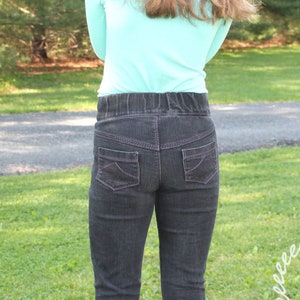 May include: A pair of dark gray jeans with a pink stitching detail. The jeans have a waistband with a belt loop detail.