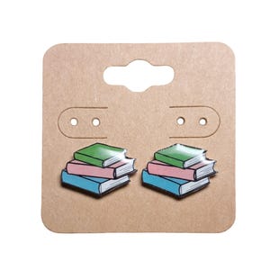 May include: A pair of book-shaped earrings with a stack of four books in green, pink, and blue. The earrings are on a brown card with holes for hanging.