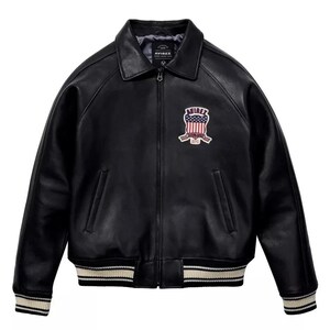 May include: Black leather jacket with a collared neckline and a zip-up front. The jacket features a patch on the chest with the text "AVIREX" and a design incorporating the American flag. The cuffs and hem have a striped design.