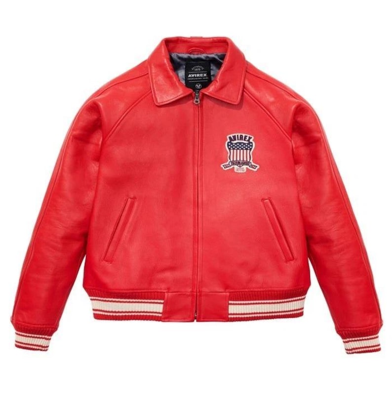Peut inclure: Veste en cuir rouge vif avec un col et une fermeture &eacute;clair. La veste pr&eacute;sente un &eacute;cusson sur la poitrine avec le texte "AVIREX" et un motif. Les poignets et l'ourlet ont des d&eacute;tails ray&eacute;s blancs et rouges.