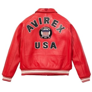 Peut inclure: Veste en cuir rouge avec le mot "AVIREX" en lettres noires sur le dos. En dessous, un &eacute;cusson circulaire avec les mots "ALL AMERICANS" et "USA". La veste a une bordure ray&eacute;e blanche et rouge.