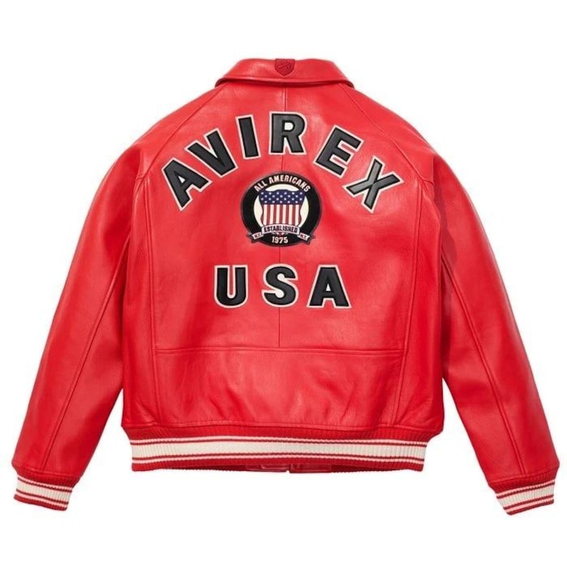 Peut inclure: Veste en cuir rouge avec le mot "AVIREX" en lettres noires sur le dos. En dessous, un &eacute;cusson circulaire avec les mots "ALL AMERICANS" et "USA". La veste a une bordure ray&eacute;e blanche et rouge.
