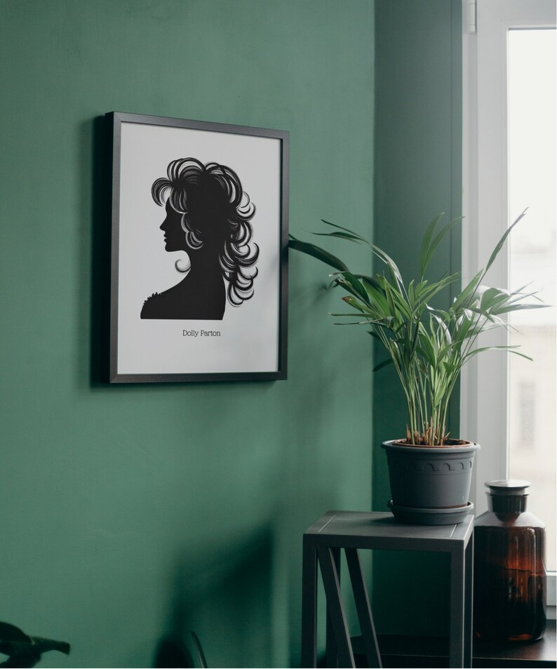 以下が含まれることがあります： 緑色の壁に額縁に入った、黒と白のシルエットのドリー・パートン。黒いサイドテーブルの上に鉢植えの植物が置かれている。