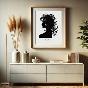 以下が含まれることがあります： 薄い茶色の壁に、ドリー・パートンのシルエットが白黒で印刷された額縁がかかっています。印刷は白い背景にされており、シルエットの下に「ドリー・パートン」という文字があります。印刷は、薄い茶色のドレッサーの上にあり、ドレッサーの上には、ドライフラワーの入った花瓶、装飾的な花瓶、本が積まれたものがあります。