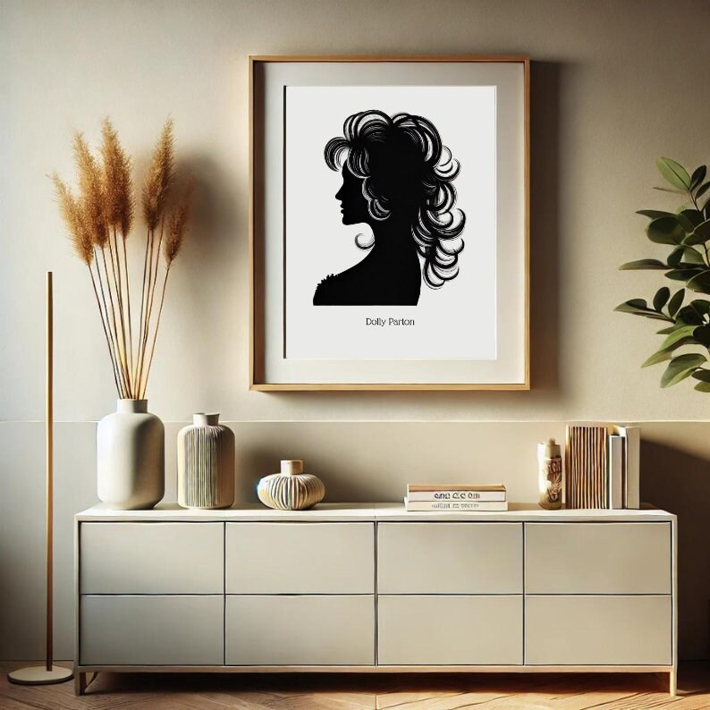 以下が含まれることがあります： 薄い茶色の壁に、ドリー・パートンのシルエットが白黒で印刷された額縁がかかっています。印刷は白い背景にされており、シルエットの下に「ドリー・パートン」という文字があります。印刷は、薄い茶色のドレッサーの上にあり、ドレッサーの上には、ドライフラワーの入った花瓶、装飾的な花瓶、本が積まれたものがあります。
