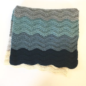 May include: A crocheted blanket with a wavy pattern in shades of blue, gray, and white.