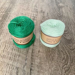 May include: Two skeins of yarn, one green and one light green, with the label "Appalachian Baby Design" on each.