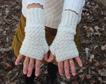 May include: Cream-colored, hand-crocheted fingerless gloves. The gloves are made with a textured stitch and have a ribbed cuff. The gloves are designed to keep hands warm while leaving fingers free. A cozy accessory for cooler weather.
