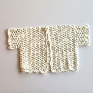 May include: A white crocheted cardigan with short sleeves and an open front.
