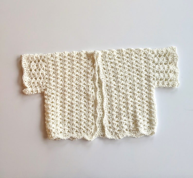 May include: A white crocheted cardigan with short sleeves and an open front.