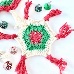 May include: A handmade crochet snowflake ornament with red, green, and cream colors. The snowflake has tassels in red and cream. Several wrapped chocolate candies are scattered around the ornament.