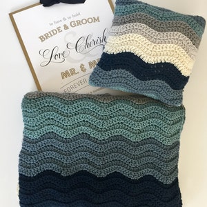 May include: A blue and green crocheted blanket with a matching pillow. The blanket and pillow have a wavy pattern. The sign in the background says "to have & to hold BRIDE & GROOM Love Cherish MR. & M FOREVER & GOODNIG"