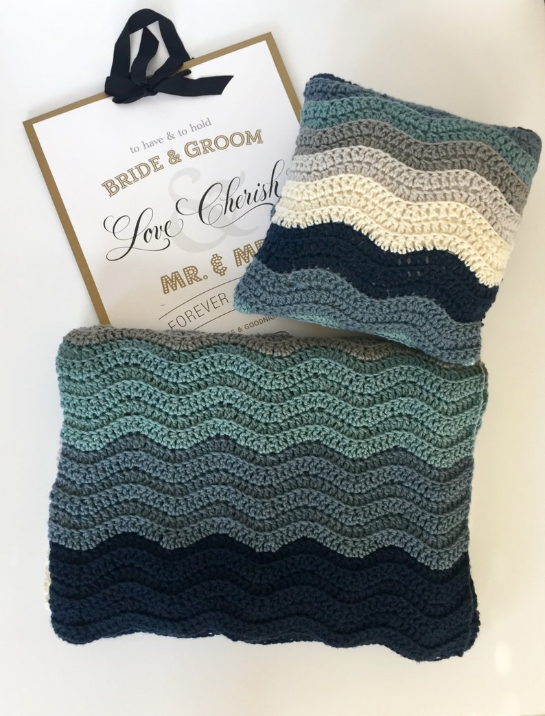May include: A blue and green crocheted blanket with a matching pillow. The blanket and pillow have a wavy pattern. The sign in the background says "to have & to hold BRIDE & GROOM Love Cherish MR. & M FOREVER & GOODNIG"