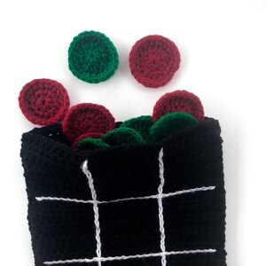 May include: A black crocheted bag with white lines forming a tic-tac-toe board. Red and green crocheted circles are scattered around the bag.