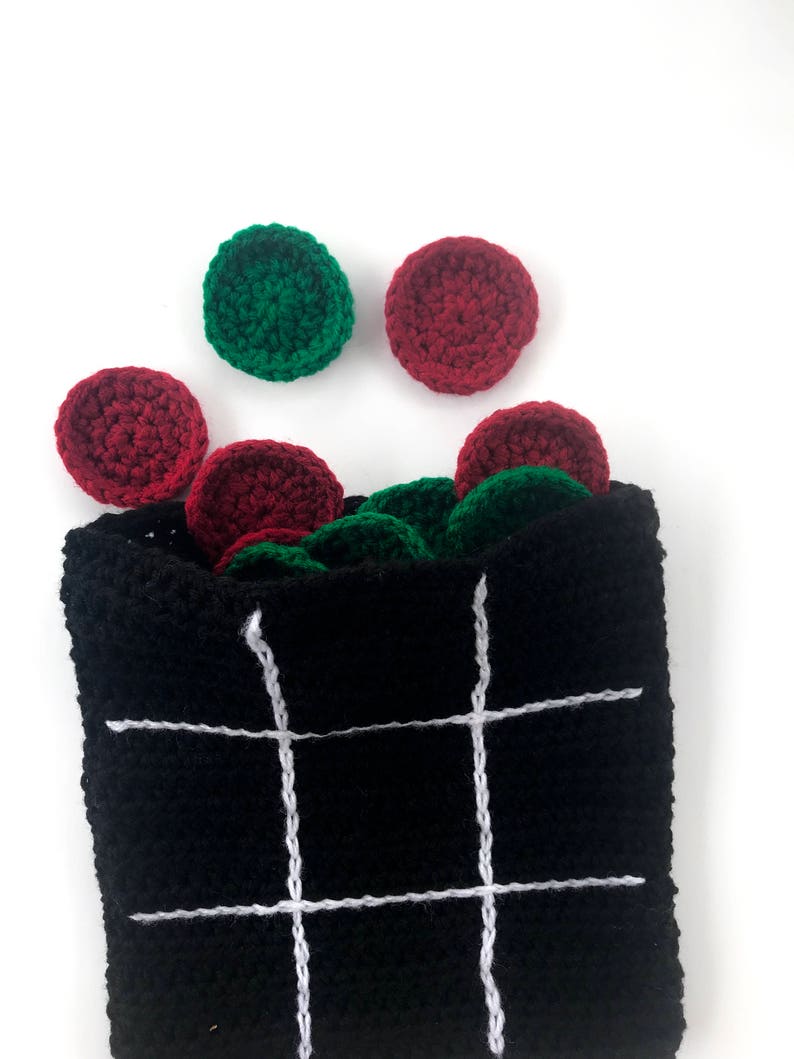 May include: A black crocheted bag with white lines forming a tic-tac-toe board. Red and green crocheted circles are scattered around the bag.