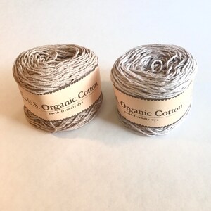 May include: Two spools of beige organic cotton yarn with brown labels that read "U.S. Organic Cotton earth-friendly dye".