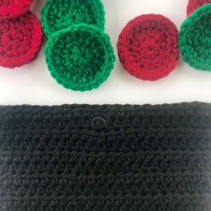 May include: A black crocheted pouch with a button closure. The pouch is surrounded by red and green crocheted circles.