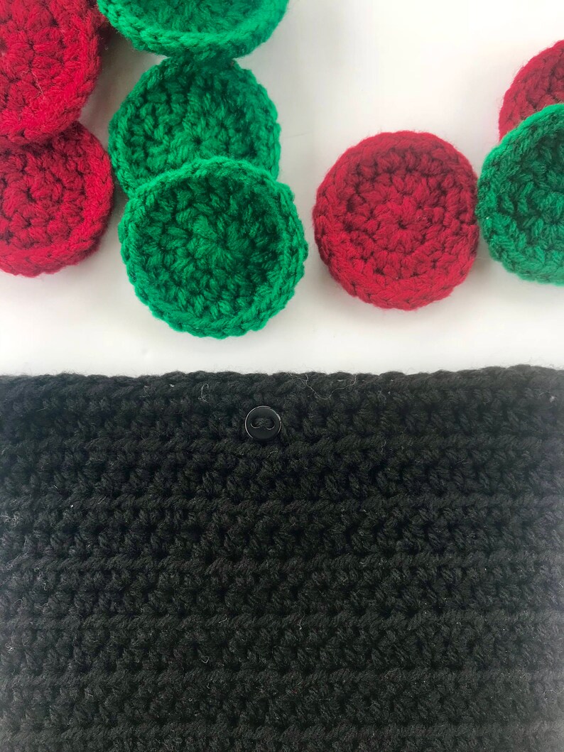 May include: A black crocheted pouch with a button closure. The pouch is surrounded by red and green crocheted circles.