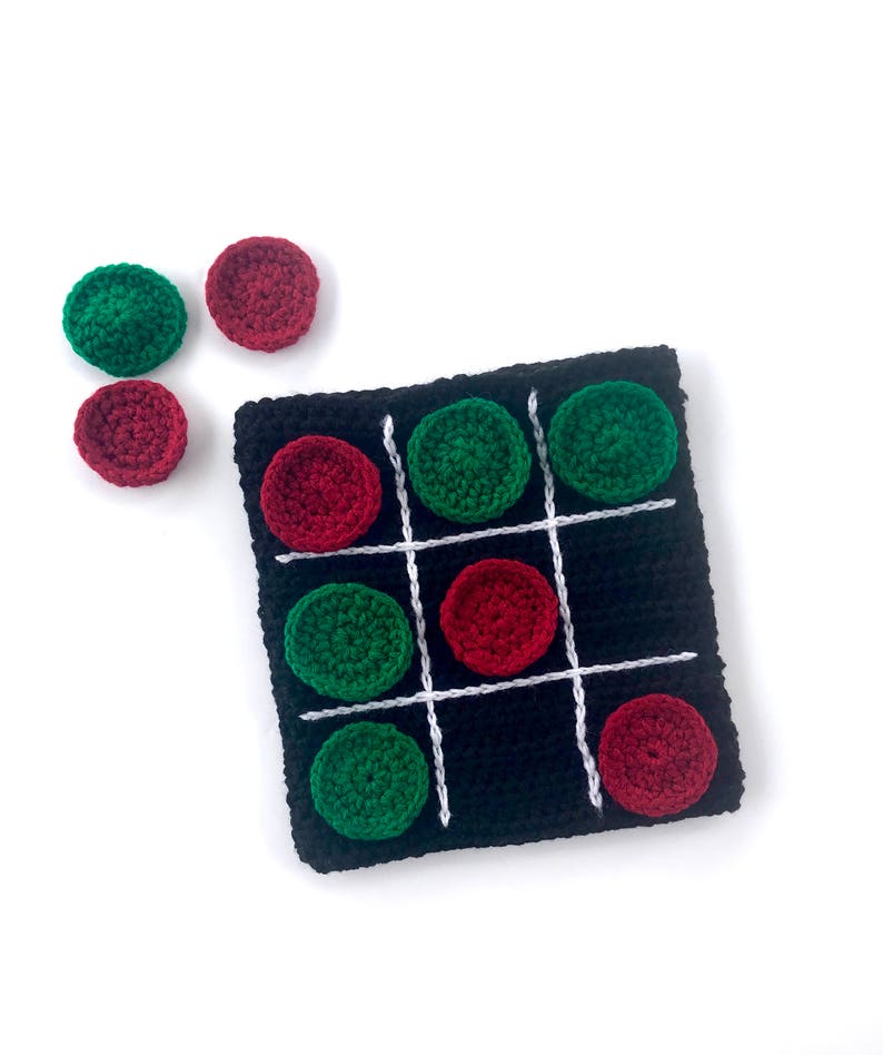 May include: A crocheted tic-tac-toe game board with red and green playing pieces. The board is black with white lines and the pieces are made of yarn.