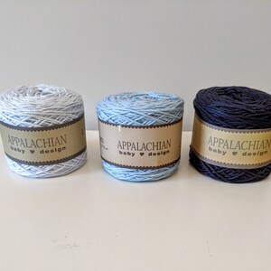 May include: Three skeins of yarn in light blue, medium blue, and navy blue. Each skein has a brown label that reads "Appalachian baby &hearts; design".