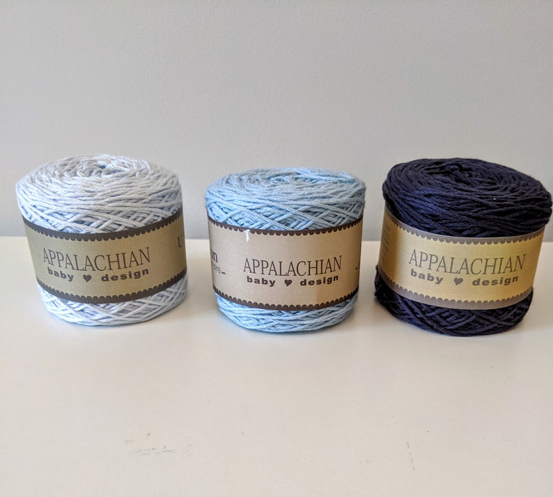 May include: Three skeins of yarn in light blue, medium blue, and navy blue. Each skein has a brown label that reads "Appalachian baby &hearts; design".