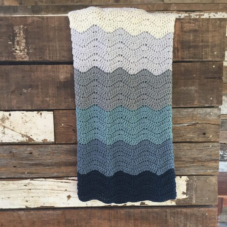 May include: A crocheted baby blanket with a wavy pattern in shades of blue, gray, and white.