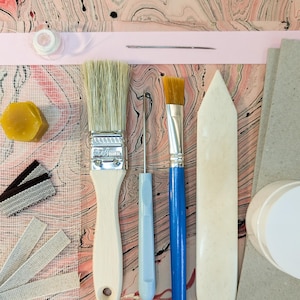 Pode incluir: Uma caneca de cerâmica branca com uma alça preta e o texto "But First, Coffee" em preto, com uma fonte manuscrita. A caneca está sobre uma superfície branca.