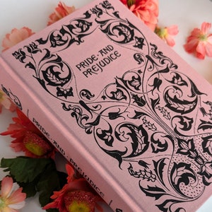 May include: A pink hardcover book with a black floral design and the title "Pride and Prejudice" on the front cover.