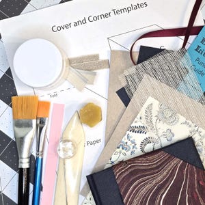 May include: A collection of craft supplies including brushes, paper, templates, and a wax seal. The image features a variety of textures and colors, including pink, beige, and blue. The text "Cover and Corner Templates" is visible.