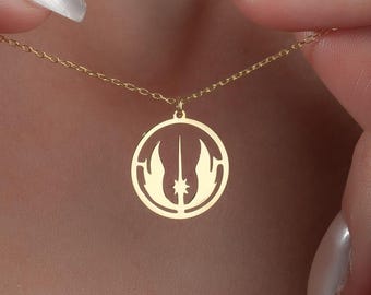 May include: A gold-colored pendant necklace featuring a circular design with a stylized symbol. The necklace is held by a person's hands, showcasing the delicate chain and pendant. The pendant's design includes a central star and two vertical elements.