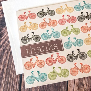 May include: A thank you card with a repeating pattern of colorful bicycles in red, orange, yellow, green, blue, and black. The word "thanks" is printed in a brown rectangle. The card is paired with a white envelope.