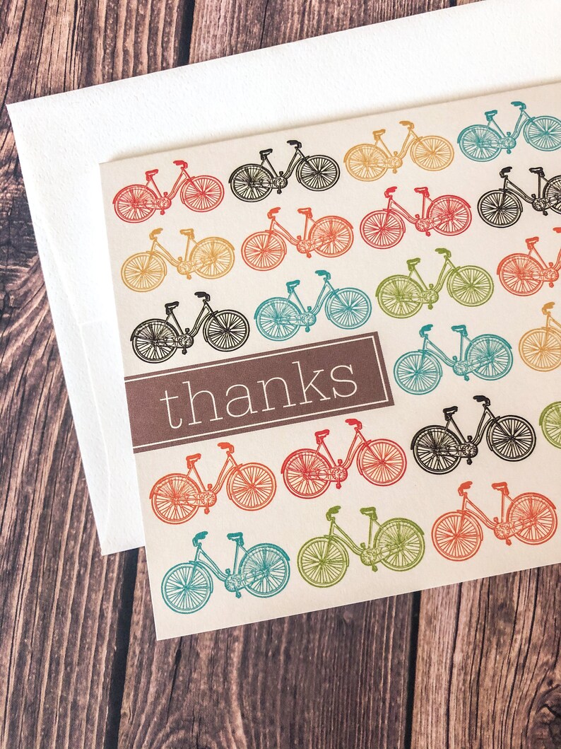 May include: A thank you card with a repeating pattern of colorful bicycles in red, orange, yellow, green, blue, and black. The word "thanks" is printed in a brown rectangle. The card is paired with a white envelope.
