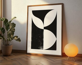 Puede incluir: Un cuadro enmarcado con un diseño geométrico abstracto en blanco y negro. La obra de arte está apoyada contra una pared, con una planta en maceta y una lámpara esférica en primer plano. El marco es de color marrón cálido.