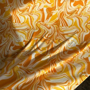 May include: A white fabric with a swirling orange and yellow marbled pattern. The fabric is draped and folded, showing the texture and design.
