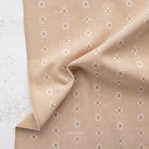 May include: A close-up of a beige fabric with a white floral pattern. The fabric is folded in half and the pattern is visible on both sides.