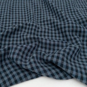 Op de afbeelding: Close-up van een blauw en zwart geruit weefsel. De stof is zacht en vloeiend, met een klassiek ruitpatroon. Het materiaal is waarschijnlijk katoen of een vergelijkbaar lichtgewicht textiel, geschikt voor kleding of woondecoratie.