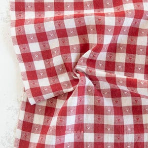 May include: Red and white checkered fabric with small heart-shaped details. The fabric is folded and draped, creating a textured appearance. The pattern is a classic gingham design, suitable for various home decor and craft projects.