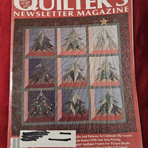 May include: The December 1991 issue of Quilter's Newsletter Magazine, number 238, features a cover image of a nine-block quilt with a Christmas tree pattern. The magazine cover includes text, a barcode, and a dark red border with a floral pattern.