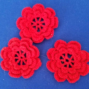 May include: Three red crocheted flowers with a center design. The flowers are made with a single crochet stitch and have a delicate, lacy appearance.