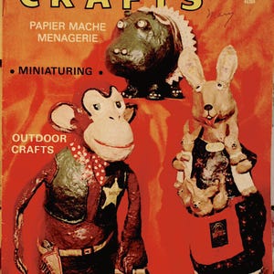 Peut inclure: Une couverture de magazine Creative Crafts de juin 1971 sur fond rouge avec trois figurines en papier mâché : un hippopotame, un singe déguisé en shérif et un lapin portant des lapereaux. Le texte indique Creative Crafts, Papier Mache Menagerie, Miniaturing et Outdoor Crafts.